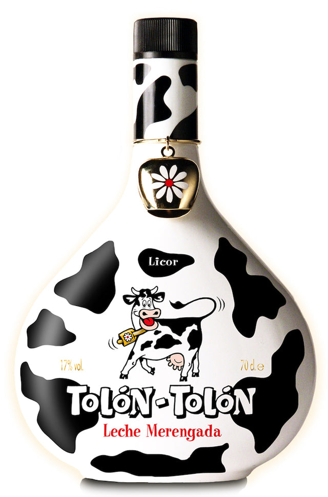 Die Flasche des Tolón-Tolón Leche Merengada Likörs in auffälligem Kuhfell-Design, verziert mit einer kleinen, goldenen Glocke mit Blütenmotiv.