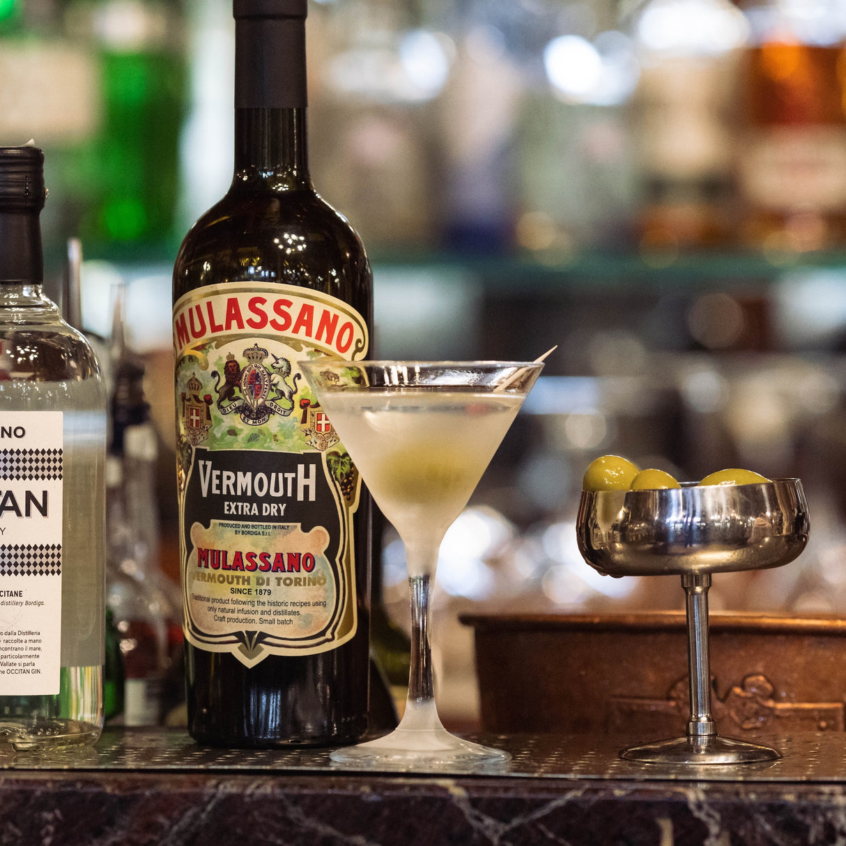 Vermouth Extra Dry Mulassano Flasche mit Martini Cocktail und Oliven in einer Bar, unscharfer Hintergrund