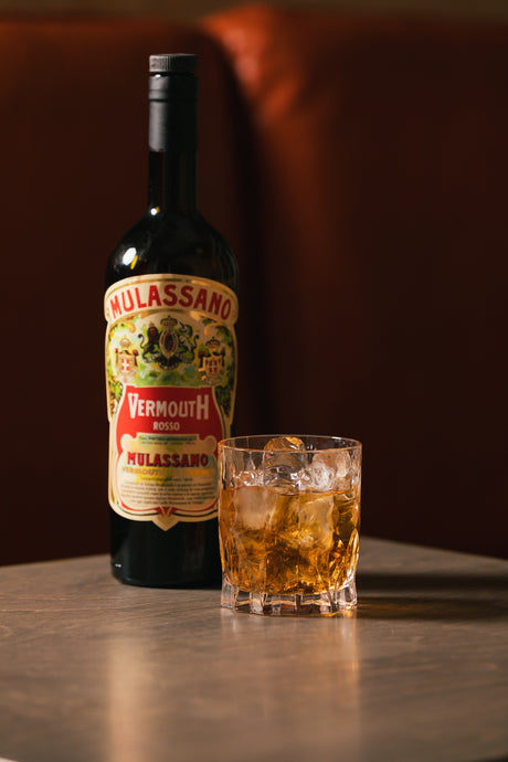 Vermouth di Torino Rosso Mulassano Flasche mit Glas auf Eis, warmes Barlicht und roter Hintergrund