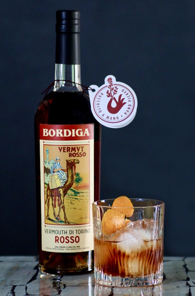 Flasche Bordiga Vermouth di Torino Rosso neben einem mit Eiswürfeln gefüllten Glas und einer Orangenschale als Garnitur.