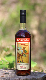 Flasche Bordiga Vermouth di Torino Rosso mit traditionellem Etikett, stehend auf einem Baumstumpf in natürlicher Umgebung.