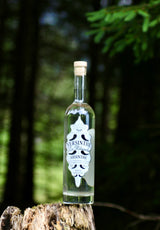 Versinthe La Blanche weißer Absinth Flasche auf Baumstumpf vor grünem Waldhintergrund