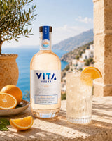 Vita Orange Wodka Flasche mit Longdrink, Orangenscheiben und mediterraner Küstenkulisse