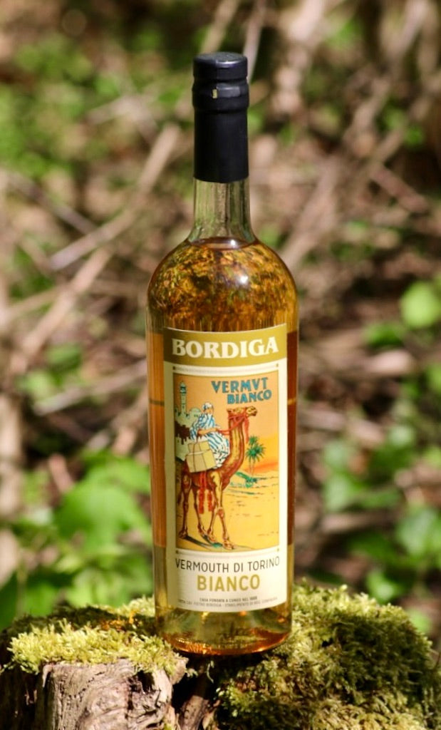 Flasche Bordiga Vermouth di Torino Bianco, 750 ml, mit schwarzem Verschluss und Vintage-Etikett, auf einem moosbedeckten Baumstumpf platziert.