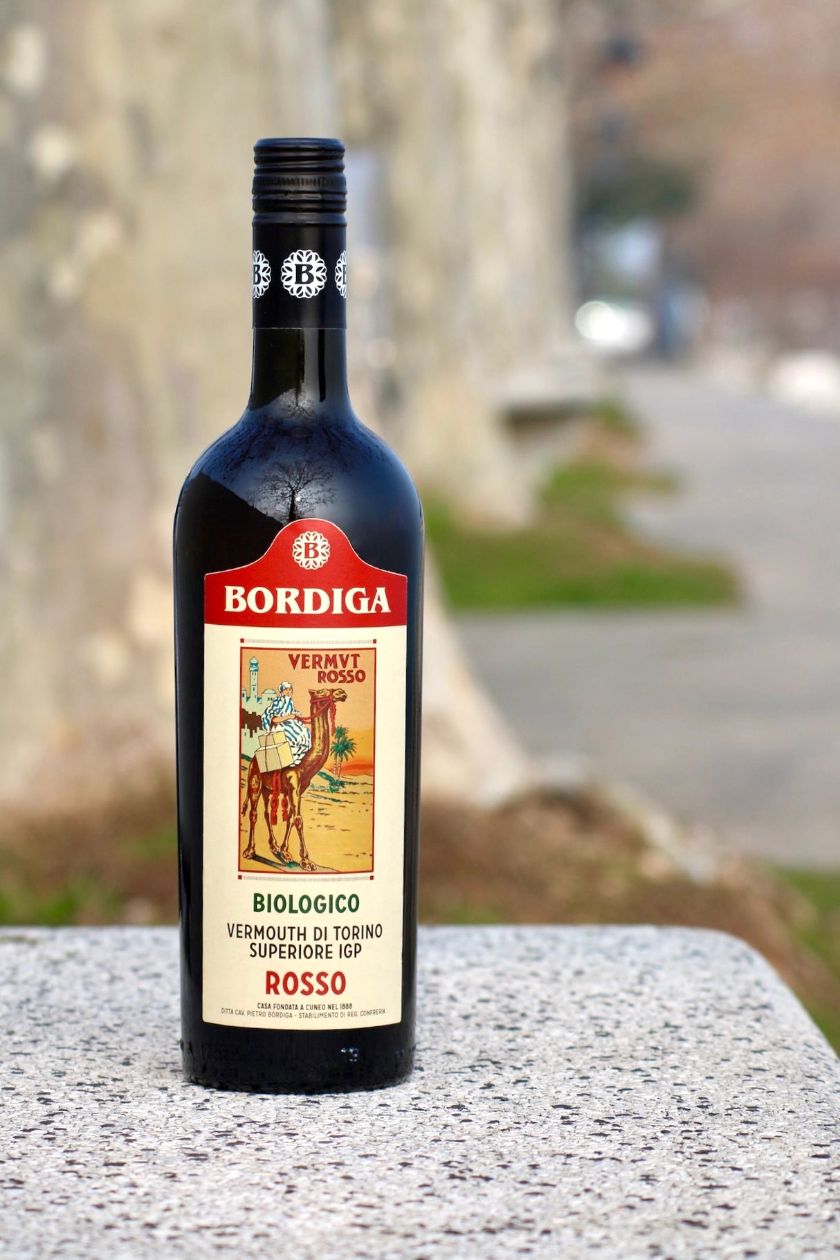 Flasche Bio-Vermouth di Torino Rosso von Bordiga auf einem Steintisch vor unscharfem Hintergrund, der eine Allee zeigt.